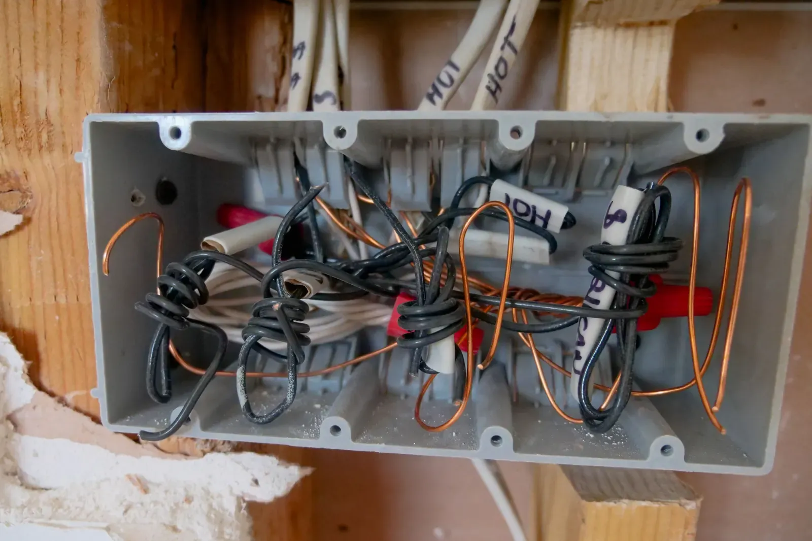 An open electrical junction box with loose, tangled wires inside an unfinished wall