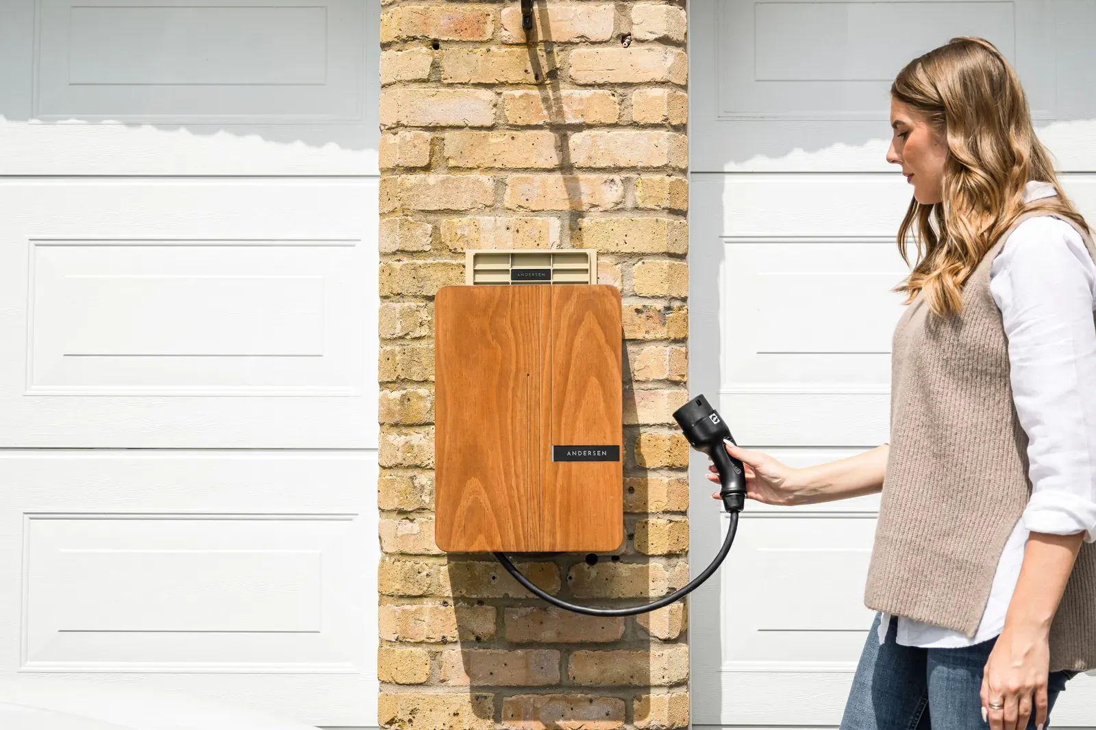 A homeowner holding the connector of a wall-mounted Level 2 EV charger in a garage