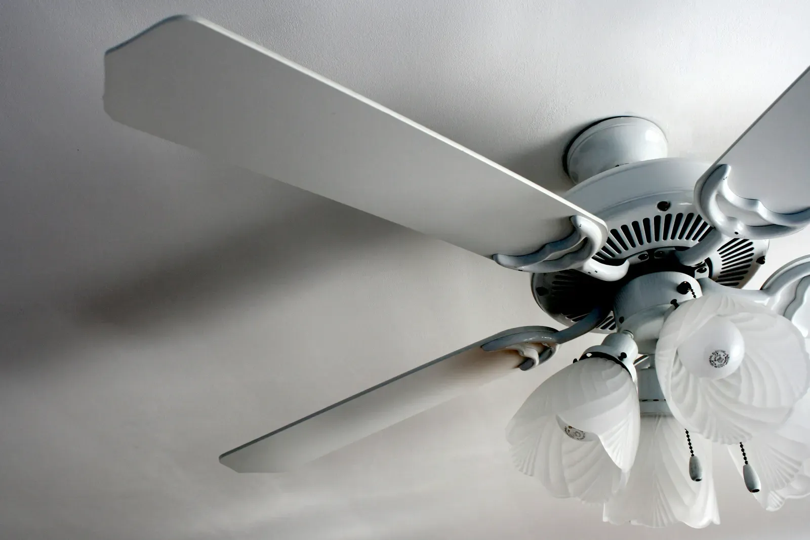 A white ceiling fan with a frosted glass light kit, seen from below against a white ceiling