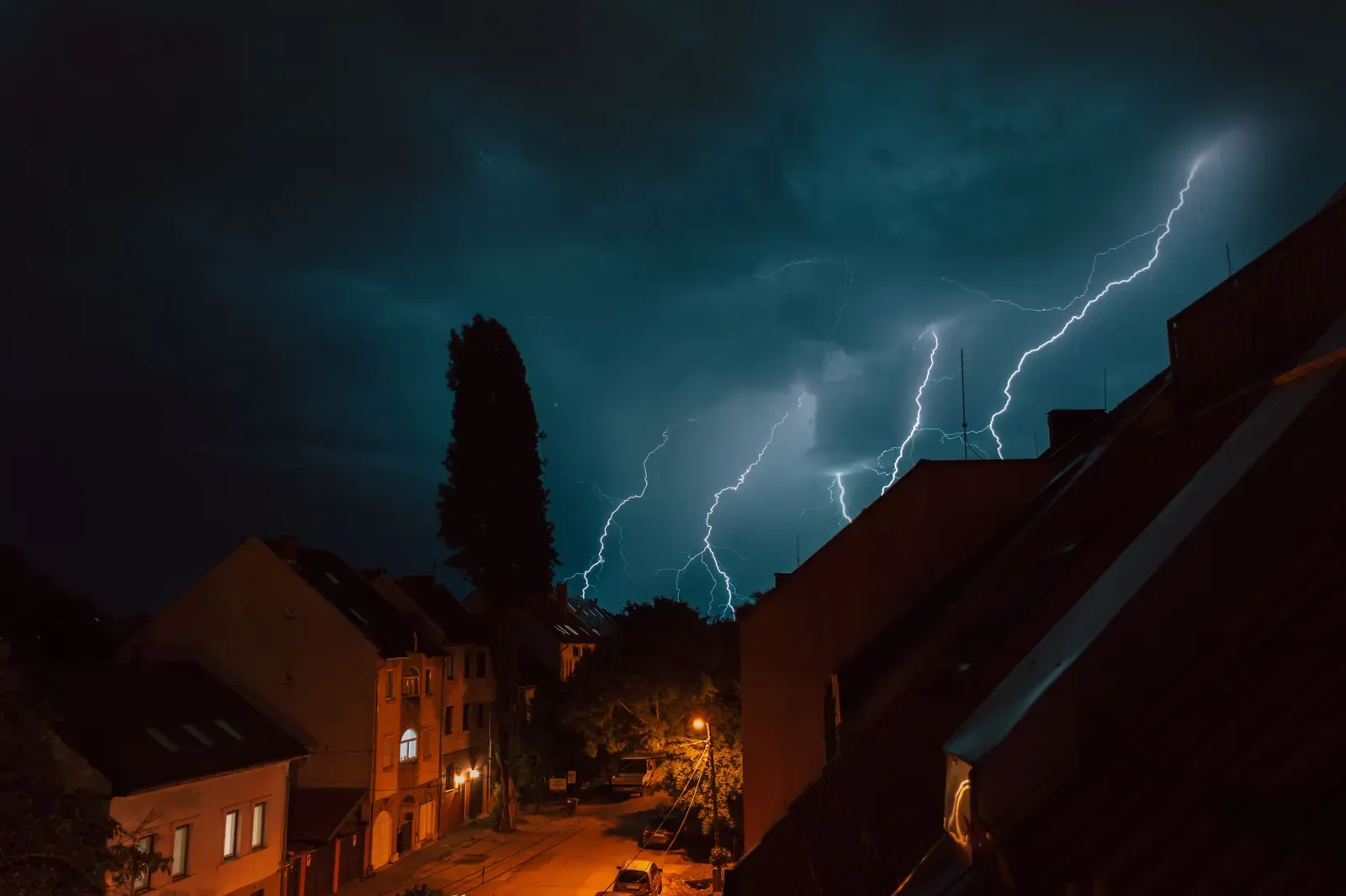 Lightning strikes over rooftops during a nighttime thunderstorm