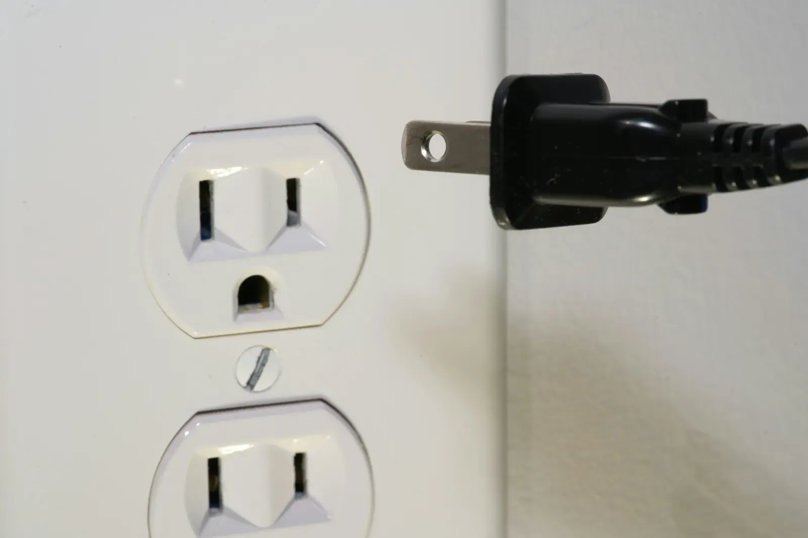 A standard U.S. three-prong duplex wall outlet with a two-prong plug beside it