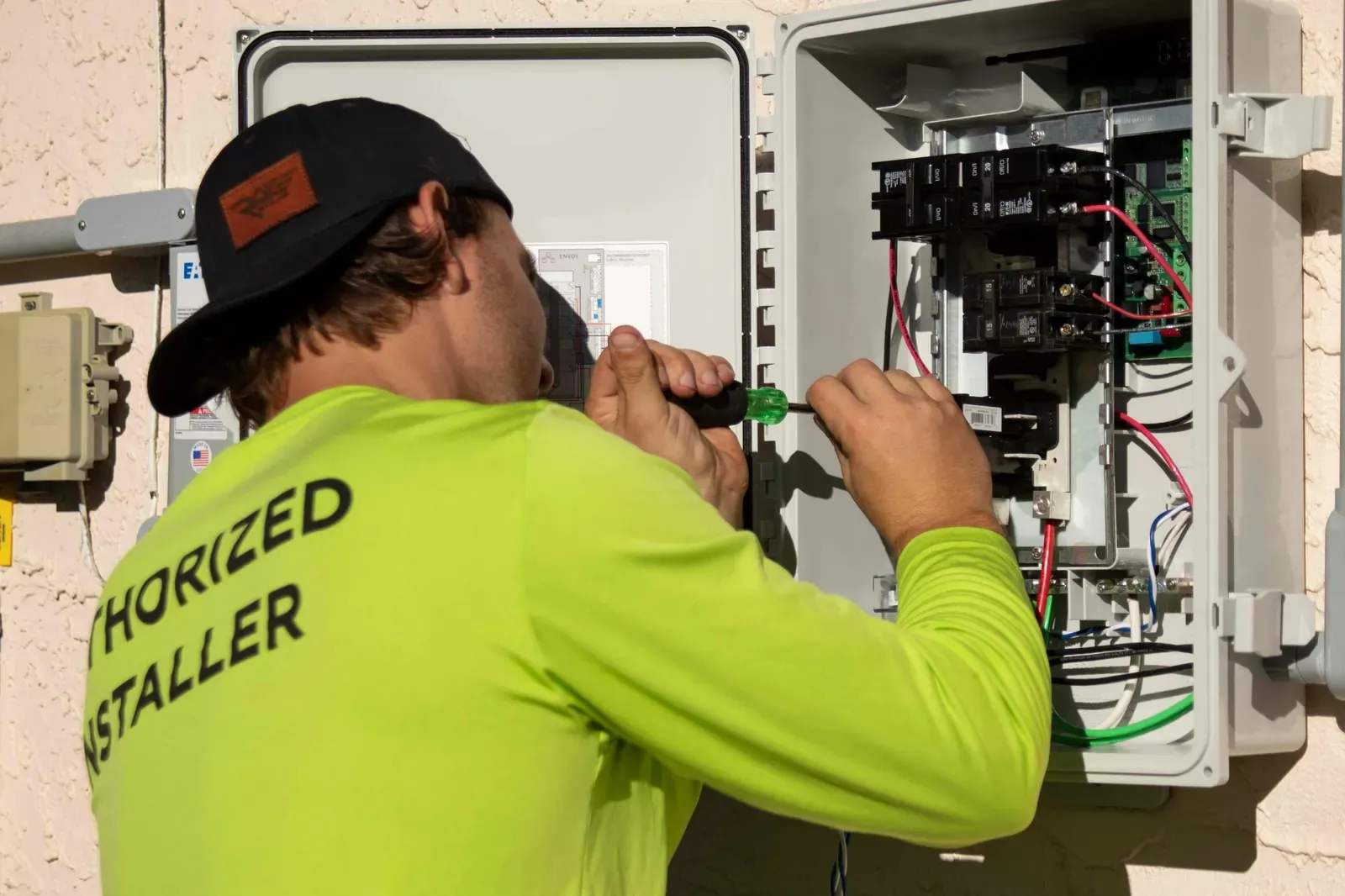 An electrician wiring an outdoor electrical panel mounted on a stucco wall